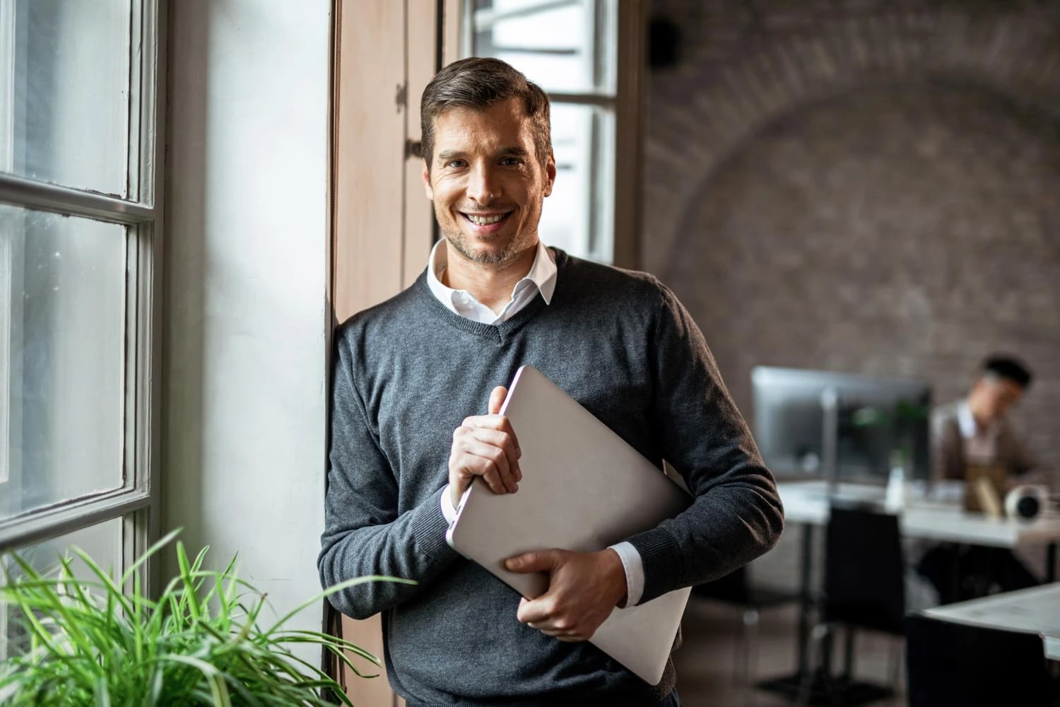 Dirigeant d'entreprise souriant tenant un ordinateur portable dans un environnement de travail professionnel